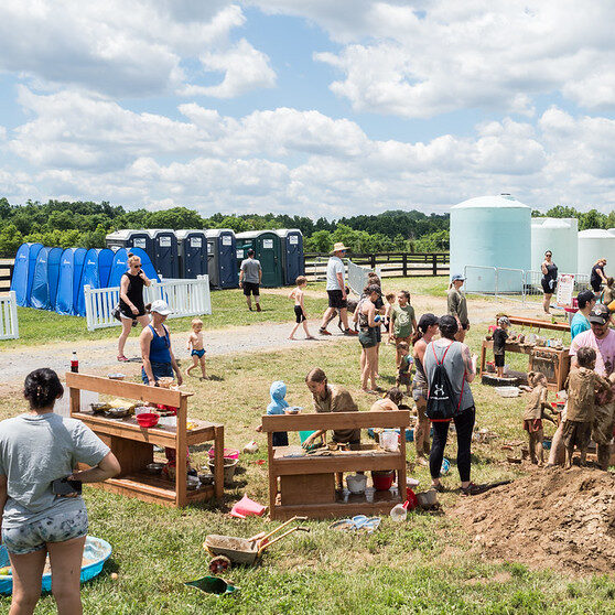 Families playing with kitchen toys in the mud and blue changing tents in the background.
