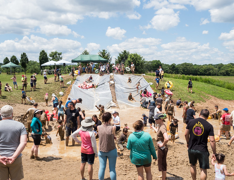 A crowd of people watching individuals slide down a muddy hill.