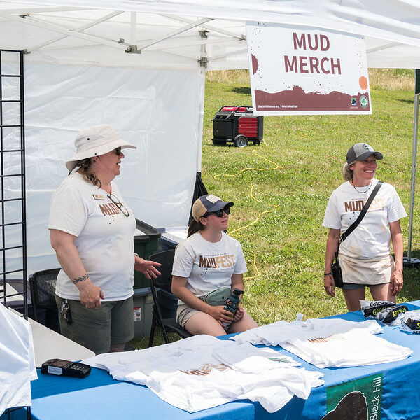 People standing behind a table of shirts with a sign above them reading "Mud Merch".