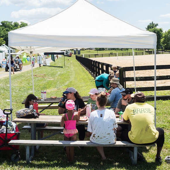 A family sitting at a picnic table under a canopy tent.