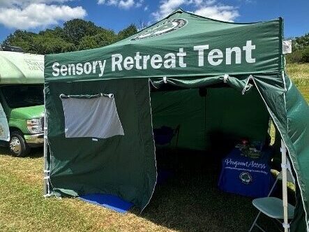 A green canopy tent with sides and an opening for a door labeled " Sensory Retreat Tent".
