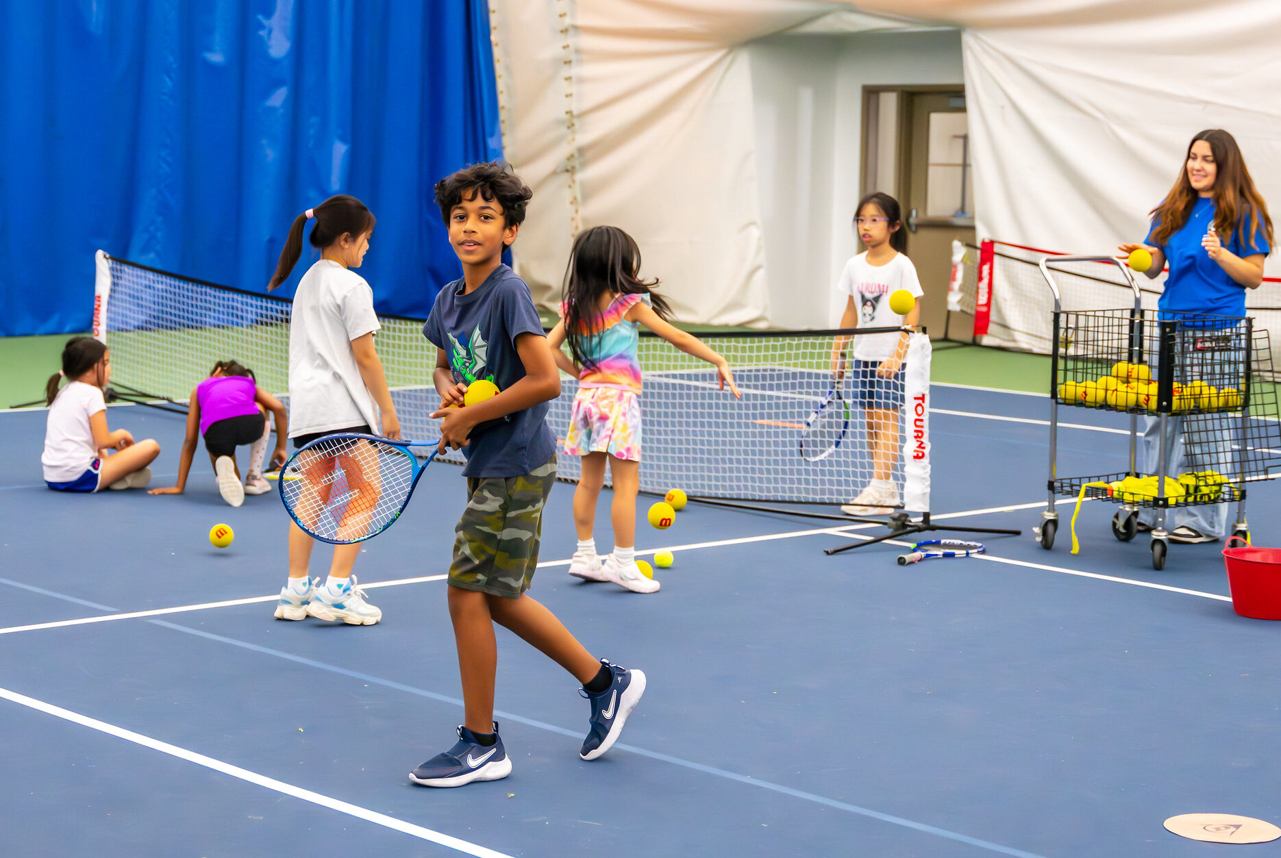 A kid smiling at the camera with a tennis raquet