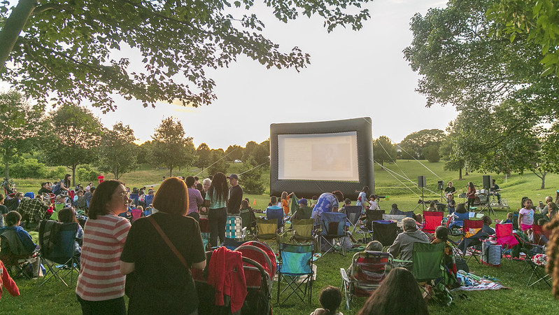 Audience sitting in front of movie screen in serene outdoor setting.