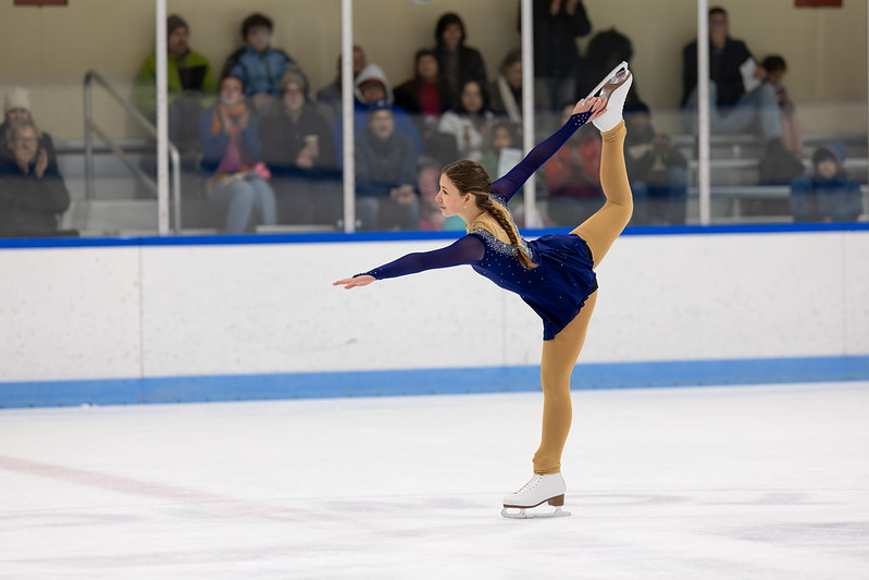Skater in blue dress performing a catch foot spiral
