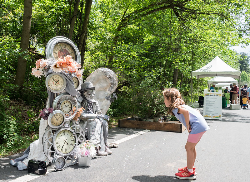 Child bending down to look at living statue wearing sliver clocks and wings