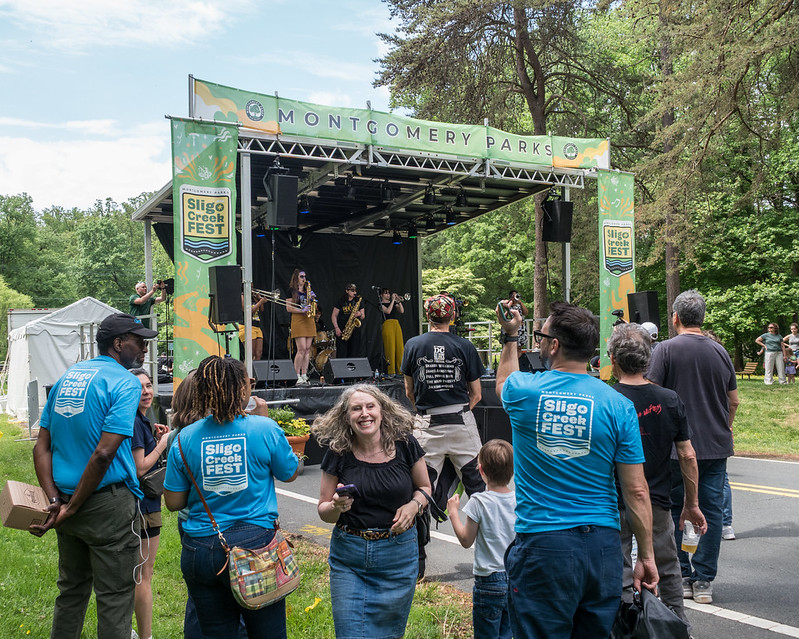 Parks Staff with blue t-shirts that have Sligo Creek Fest 2025 logo on the back of them watch main stage