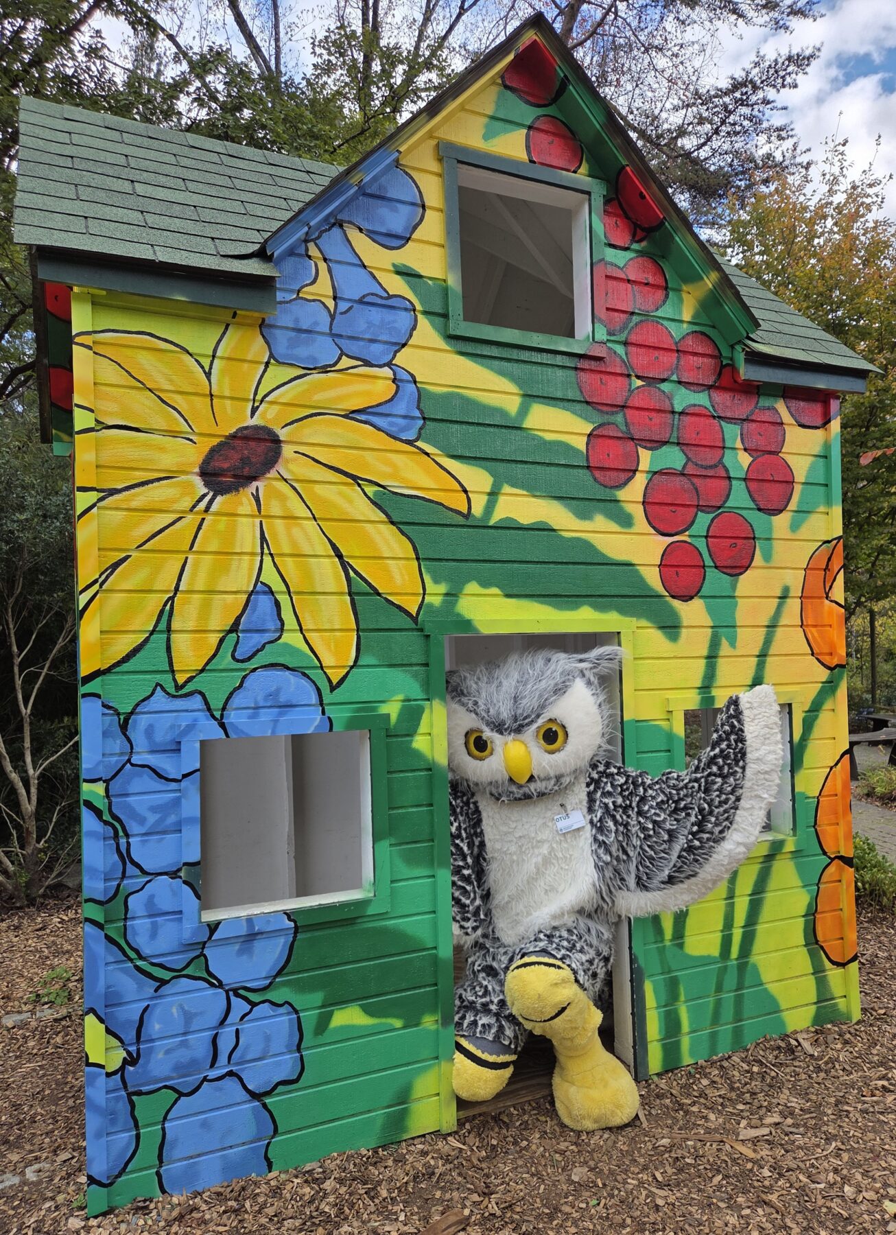 Otus, the Owl Mascot at Montgomery Parks, is pictured waving from the entrance of the freshly painted play house in the garden.