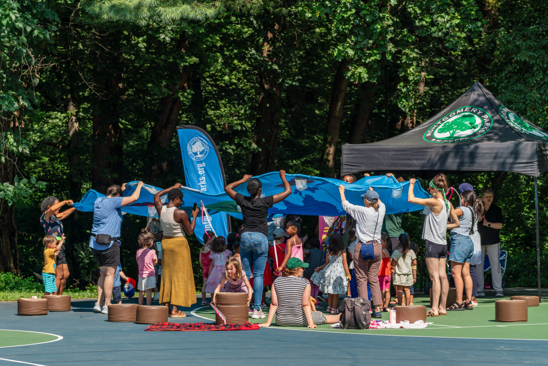 Parents hold up parachute toy while children play underneath