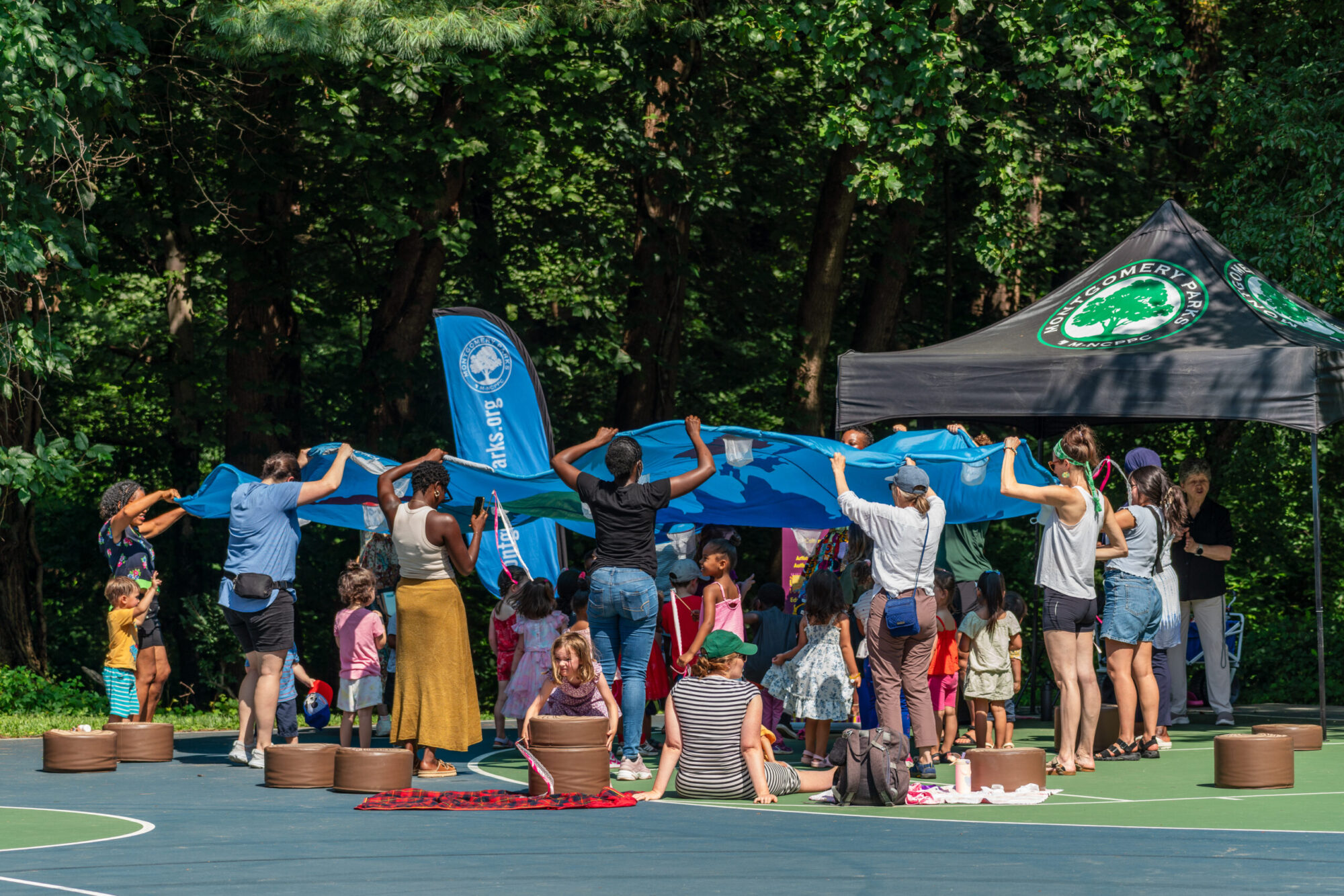 Parents hold up parachute toy while children play underneath