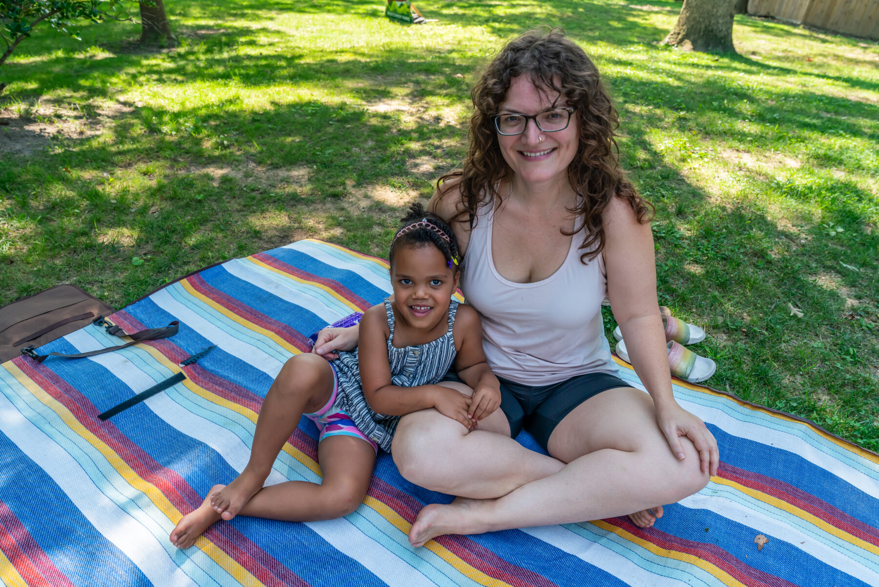 Parent and child smile for camera on picnic blanket on the lawn