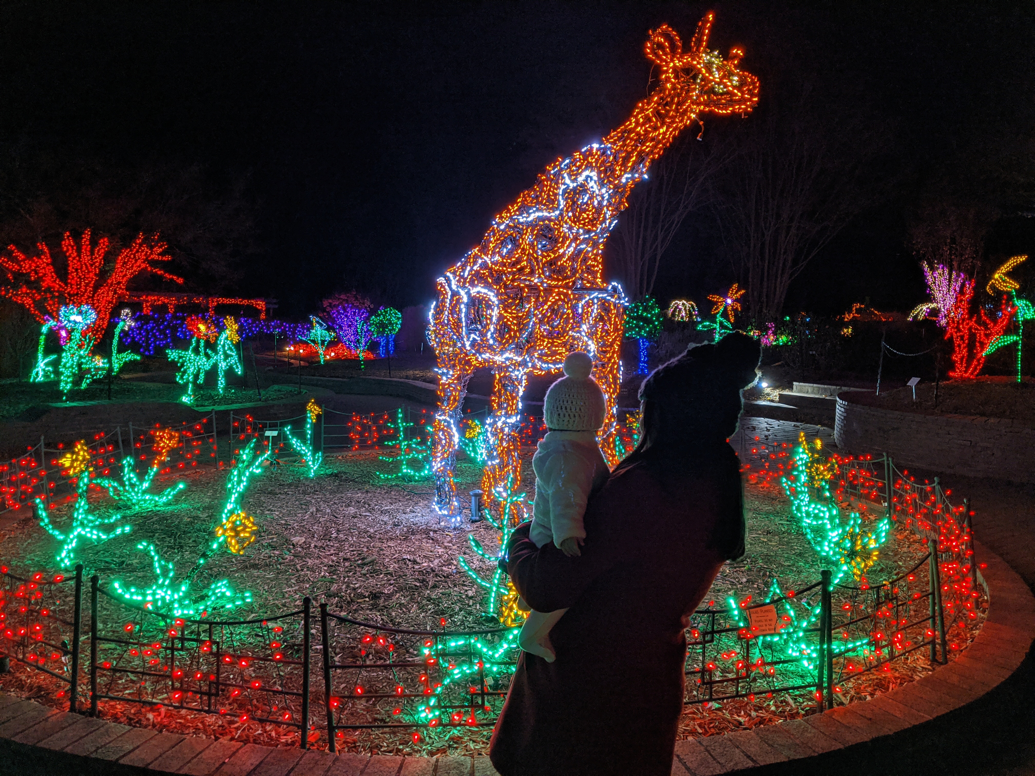 A parent and child in front of a giraffe light structure