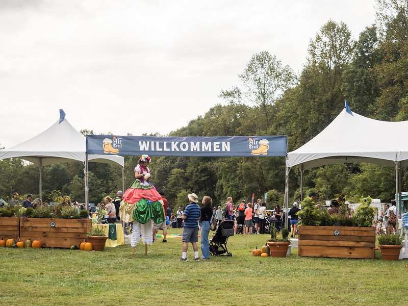 "Willkommen" banner at Parks Ale Trail entrance with stilt walker greeting people