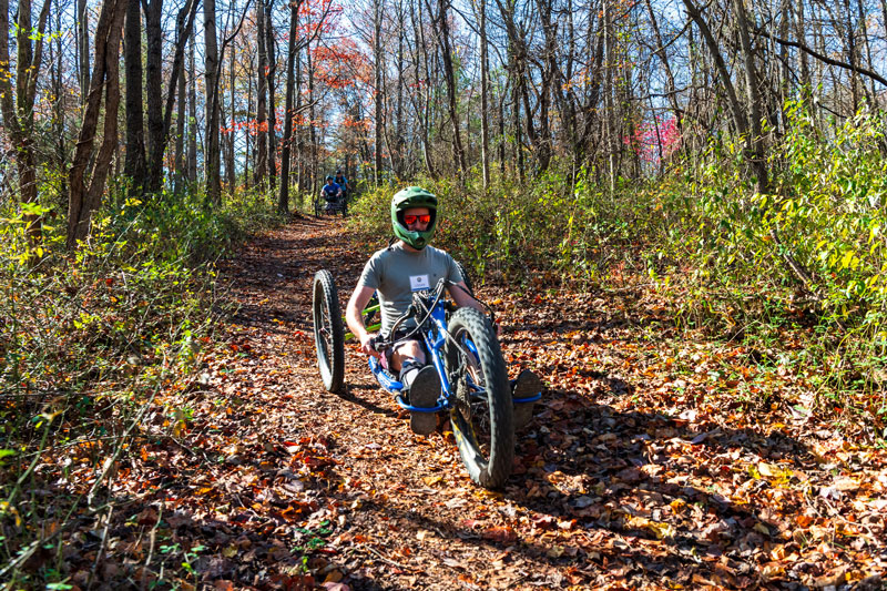 Man with helmet and sunglasses riding hand-powered recumbent mountain bike