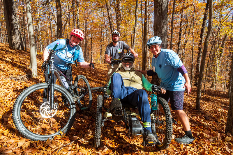 Group of people posing on a park trail with helmets and bikes man in the center has a