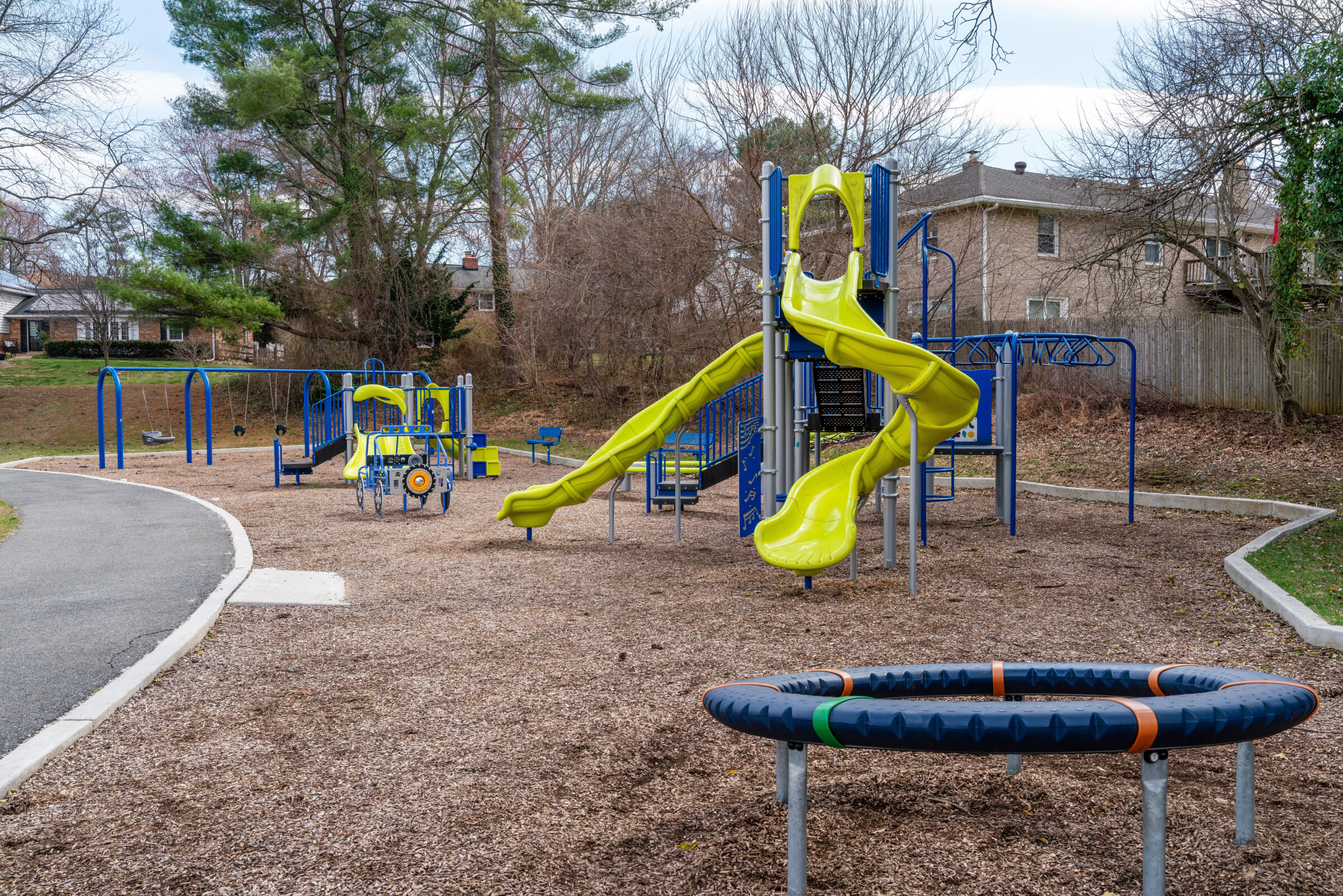 Playground at Olney Family with a balance ring, 5-2 playground set with 2 slides, monkey bars, 2-5 playground set with double slides, a play truck, and a swing set.