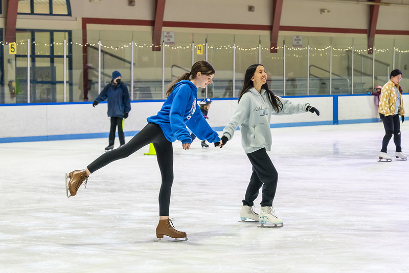 Two people holding hands while skating at Cabin John Ice Arena. One has a leg lifted behind them.