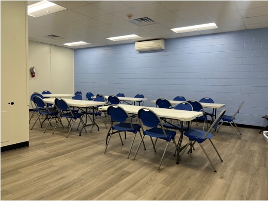 The party room with four long white tables and blue chairs at each