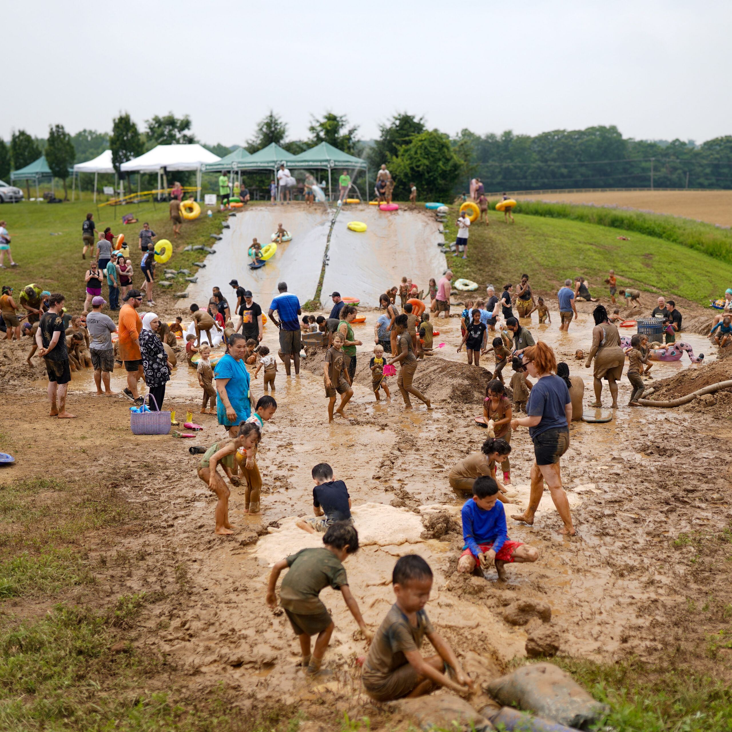 People playing in a muddy field and sliding down two mudslides using pool floats.