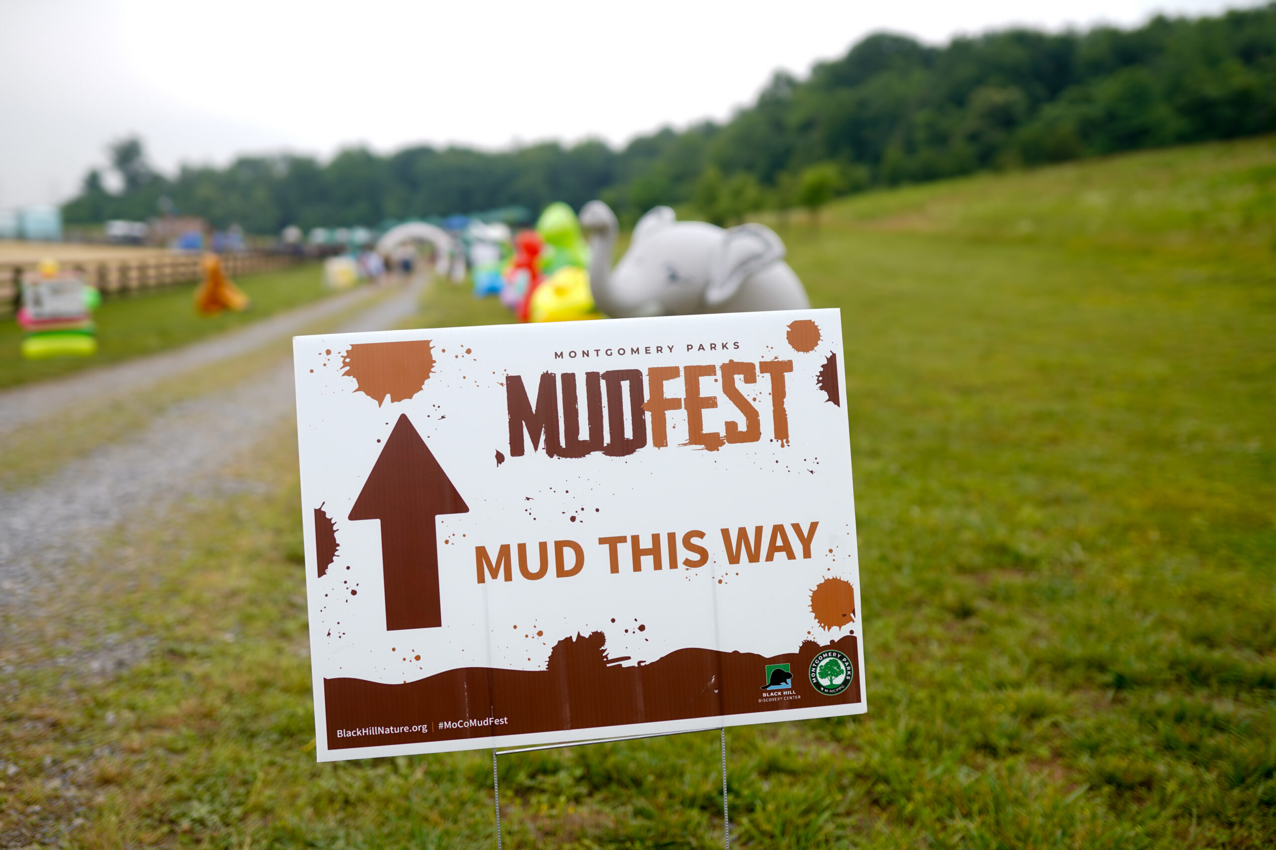 A sign standing in the grass that says MudFest Mud This Way.