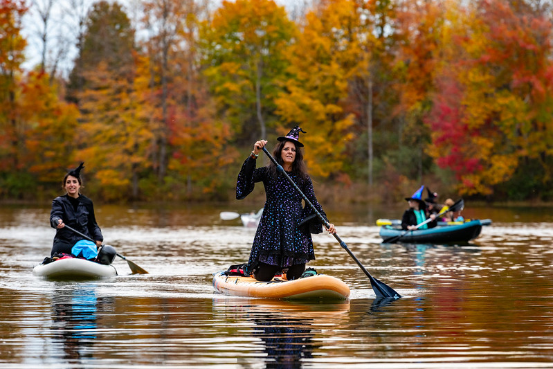 Attendees in witch costumes paddle and kayak on the lake