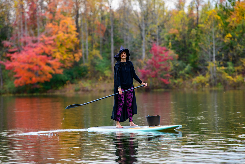 Attendee paddles on paddleboard wearing witch costume