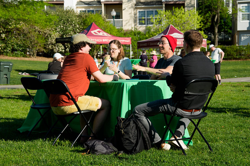 Attendees sit at table talking and eating ice cream in the park