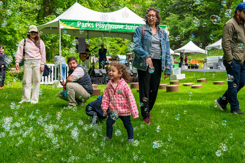 Kid smiles while bubbles float all around in grassy area with stage behind