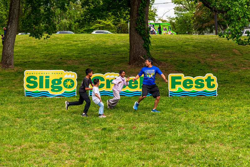 Family runs across Sligo Creek Fest letters in grassy area
