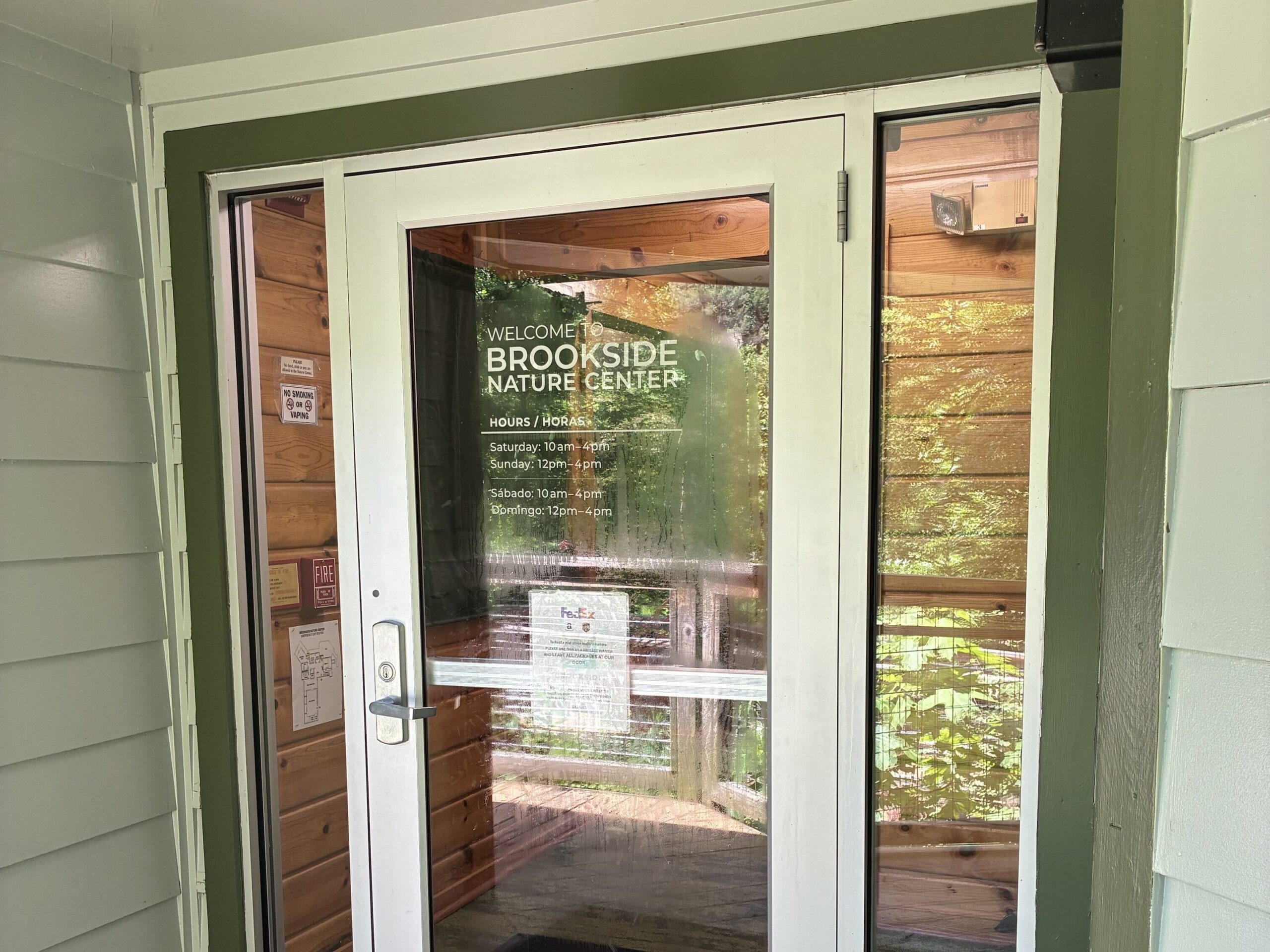 Glass door with silver metal framing and the name of the building in the center of the door with the hours below it