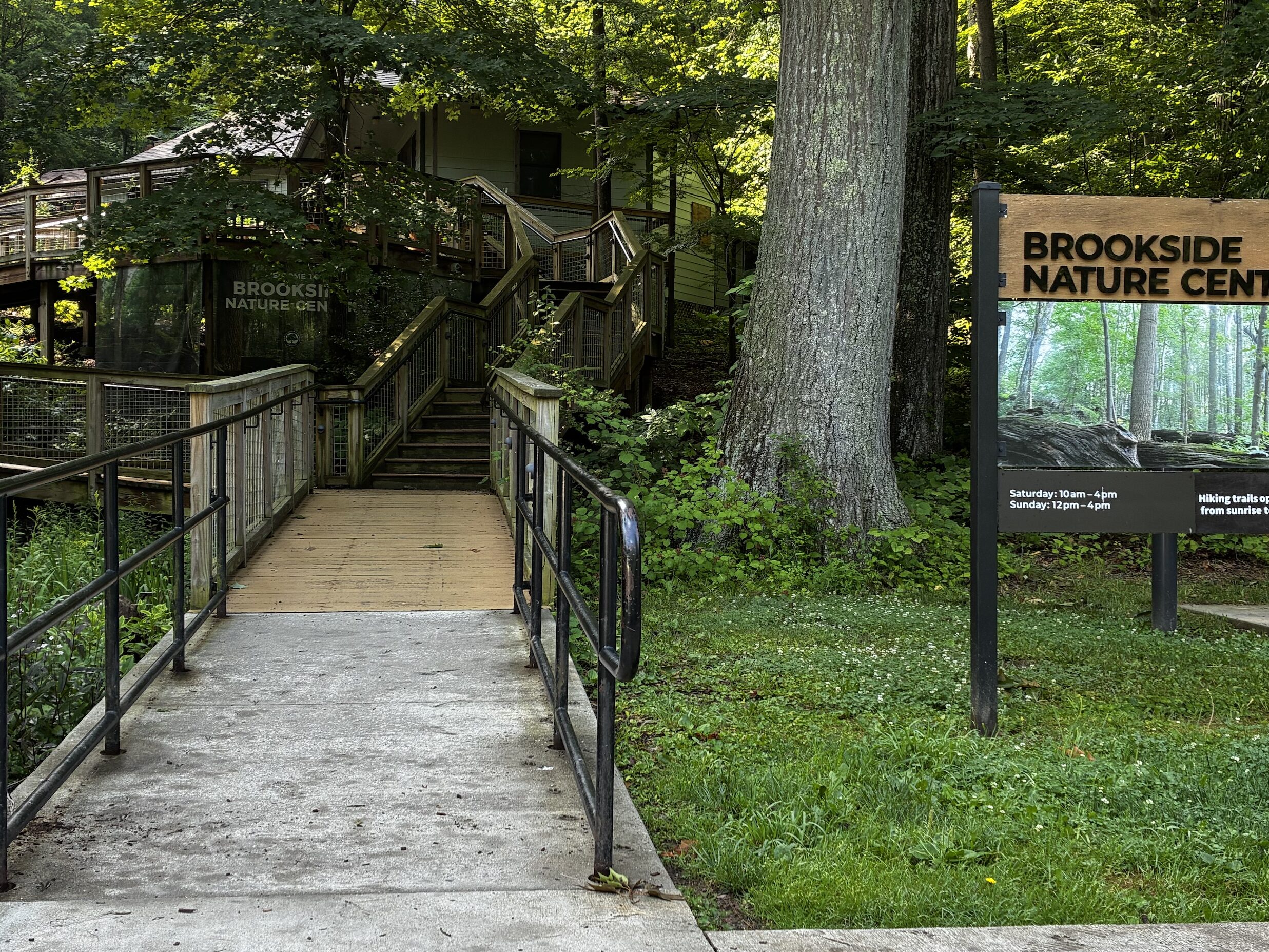 The bottom of brookside nature center steps with the welcome sign to the right that has the location name and hours of the building