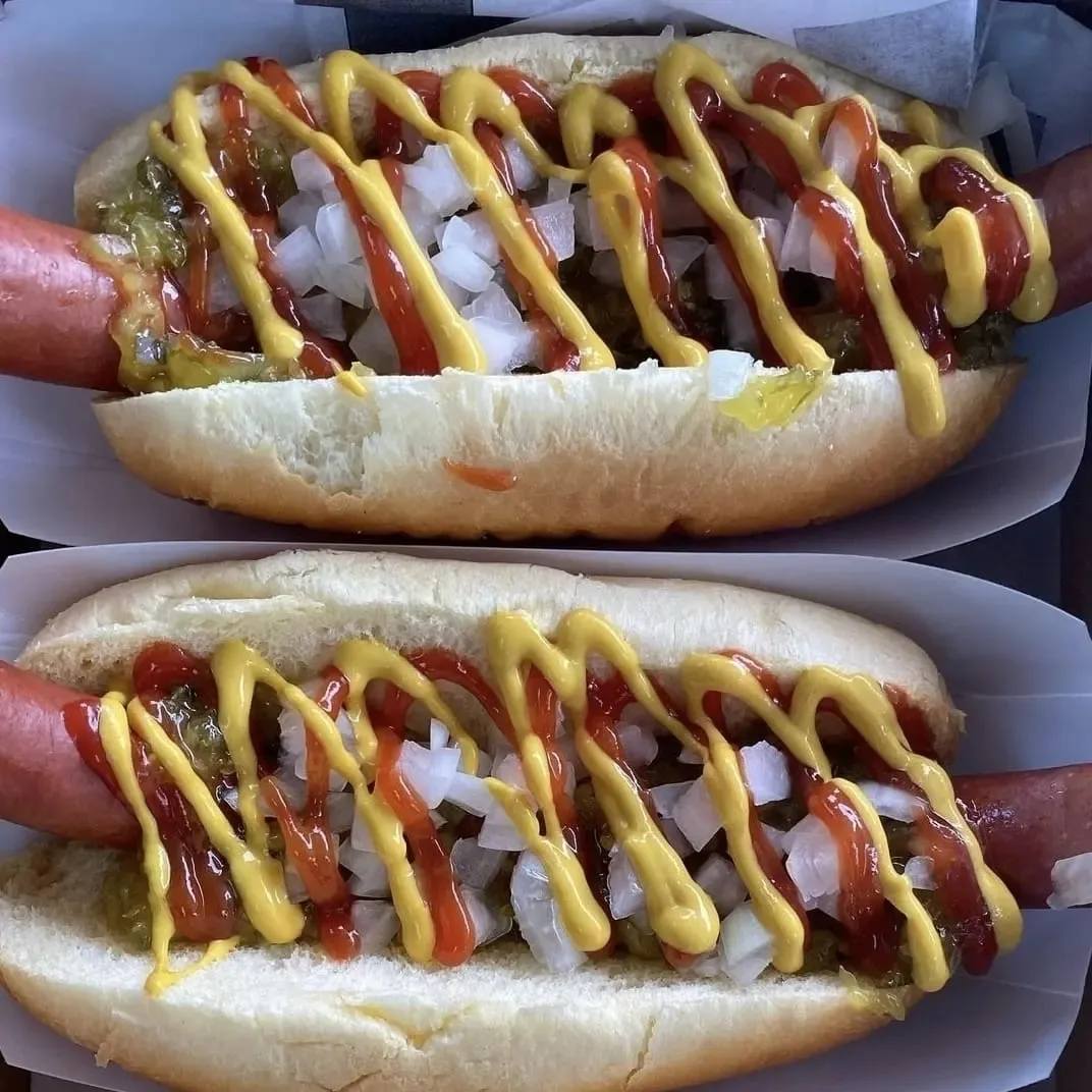 Two hotdogs with buns and relish toppings.