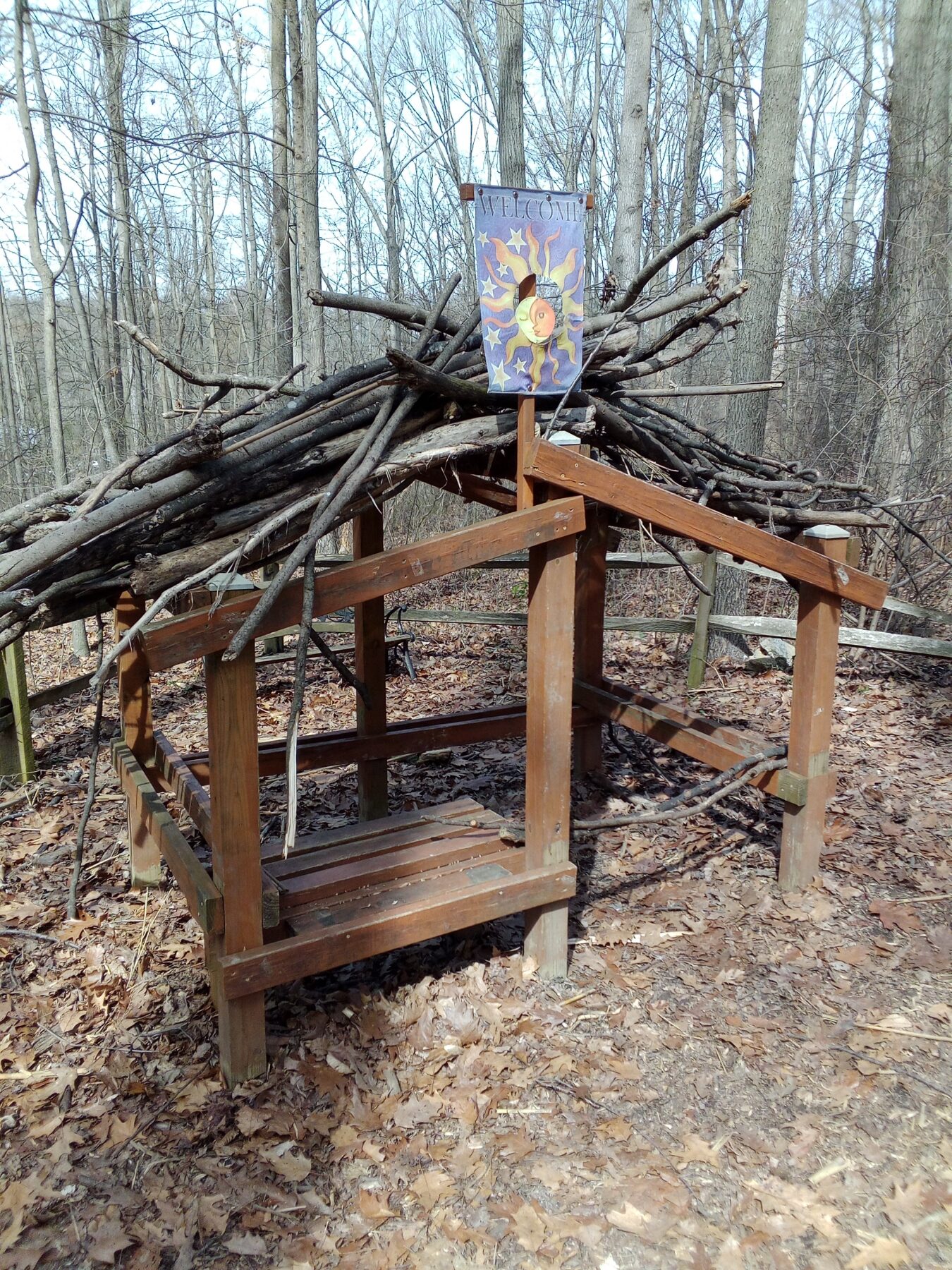 wooden playhouse with large sticks on top serving as a "roof"