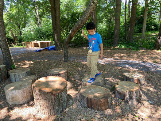 A young boy playing on stepping logs outside