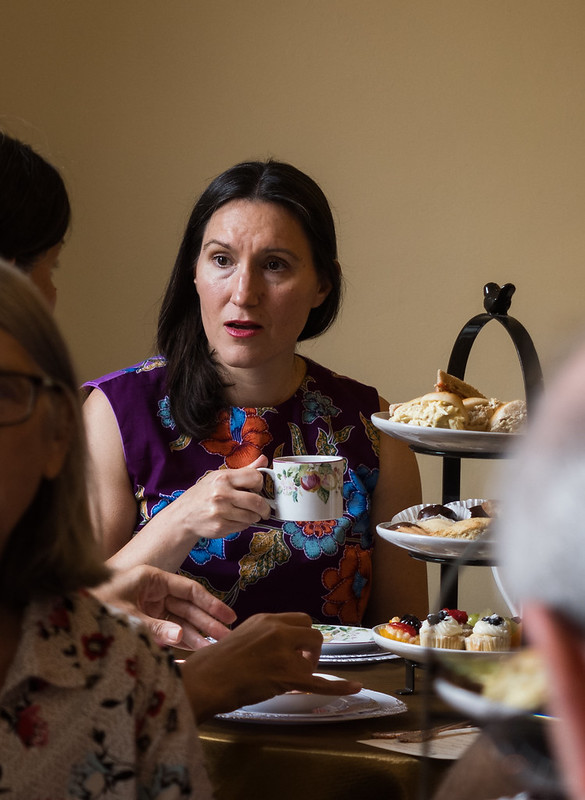 Woman in conversation holding tea cup at table with tea savories.