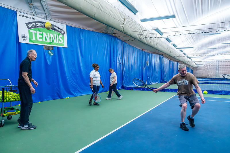 Man playing tennis with an instructor watching