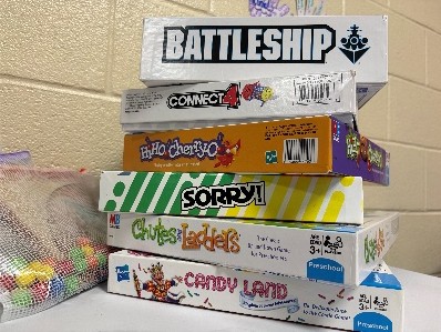 A close up of a stack of board games sitting on a table (from top to bottom; Battleship, Connect 4, Hi ho cherry-o, Sorry! Chutes & Ladders, Candy Land)