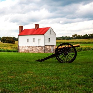Small house with red roof in the distance of an open field with refurbished canon in the foreground