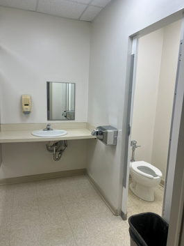 A picture of a toilet to the right side of the bathroom behind a doorway with a sink and mirror above it to the left of the doorway
