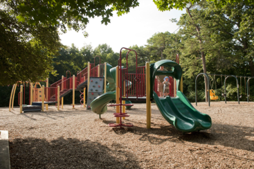 A playground with two green slides in the foreground and swings and other activities in the background