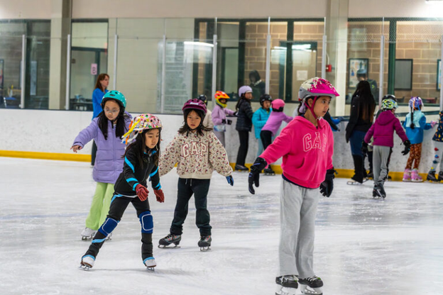 A group of kids learning how to skate on an ice rink