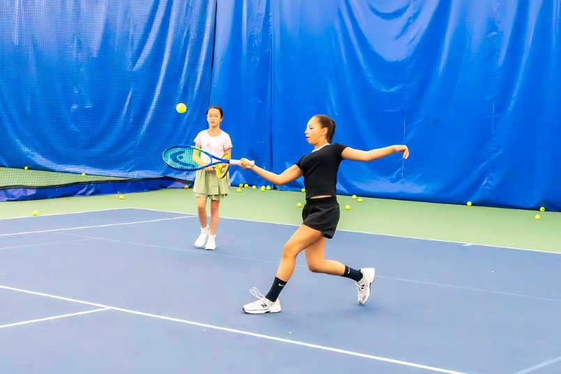 Two girls playing tennis at an indoor court