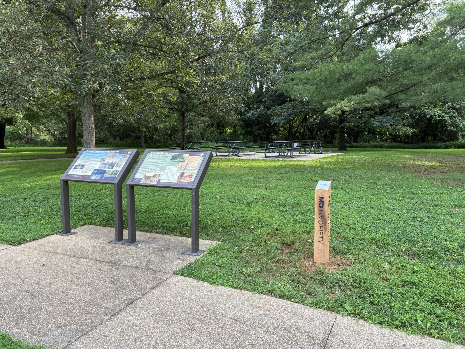 park setting with trees, concrete path and wooden post next to two educational signs