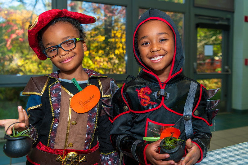 Two children in costumes holding small potted plants.